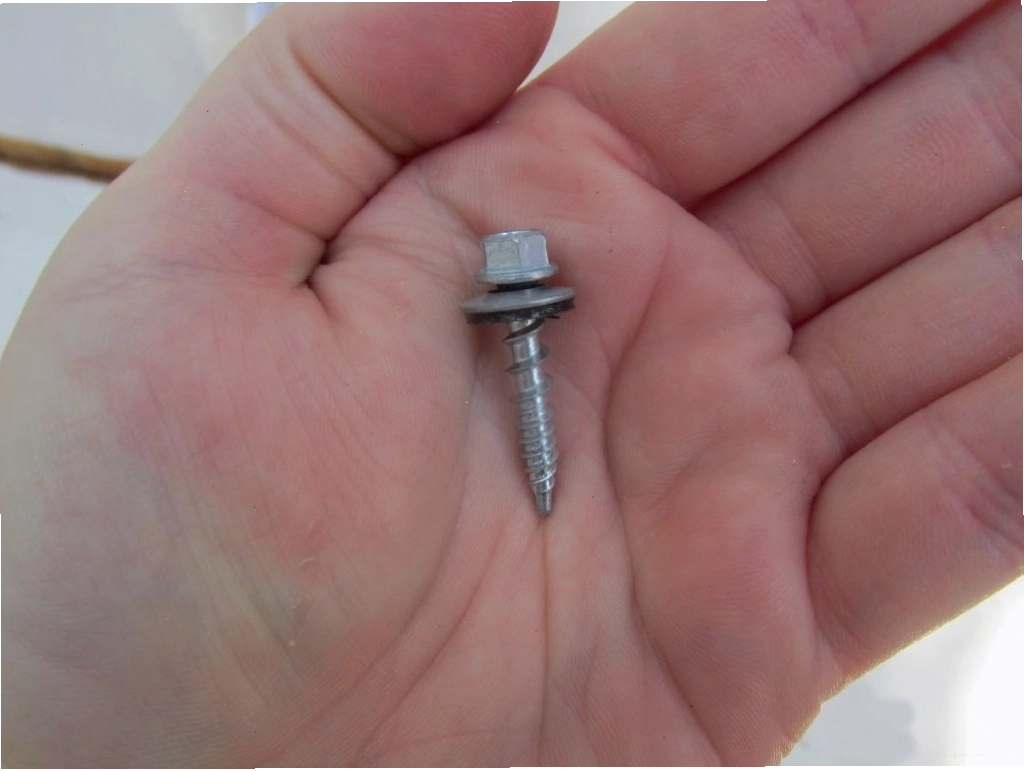 Bàn tay đang cầm một con vít tự khoan, chuẩn bị lắp đặt mái che