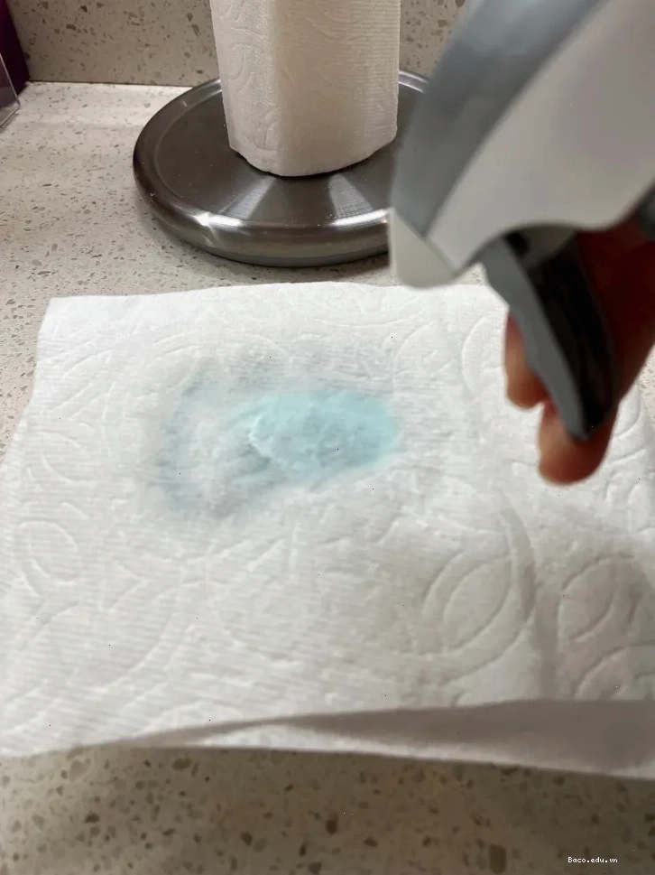 Một người đang xịt dung dịch lau kính lên giấy ăn.