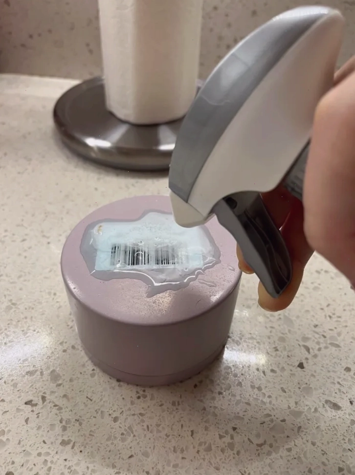 Một người đang xịt dung dịch lau kính lên nắp chai có dán nhãn.