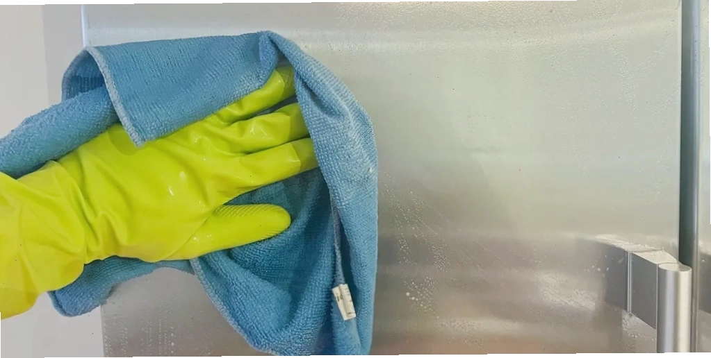 Một người đeo găng tay cao su màu vàng dùng khăn microfiber màu xanh lau bếp bằng thép không gỉ với xà phòng